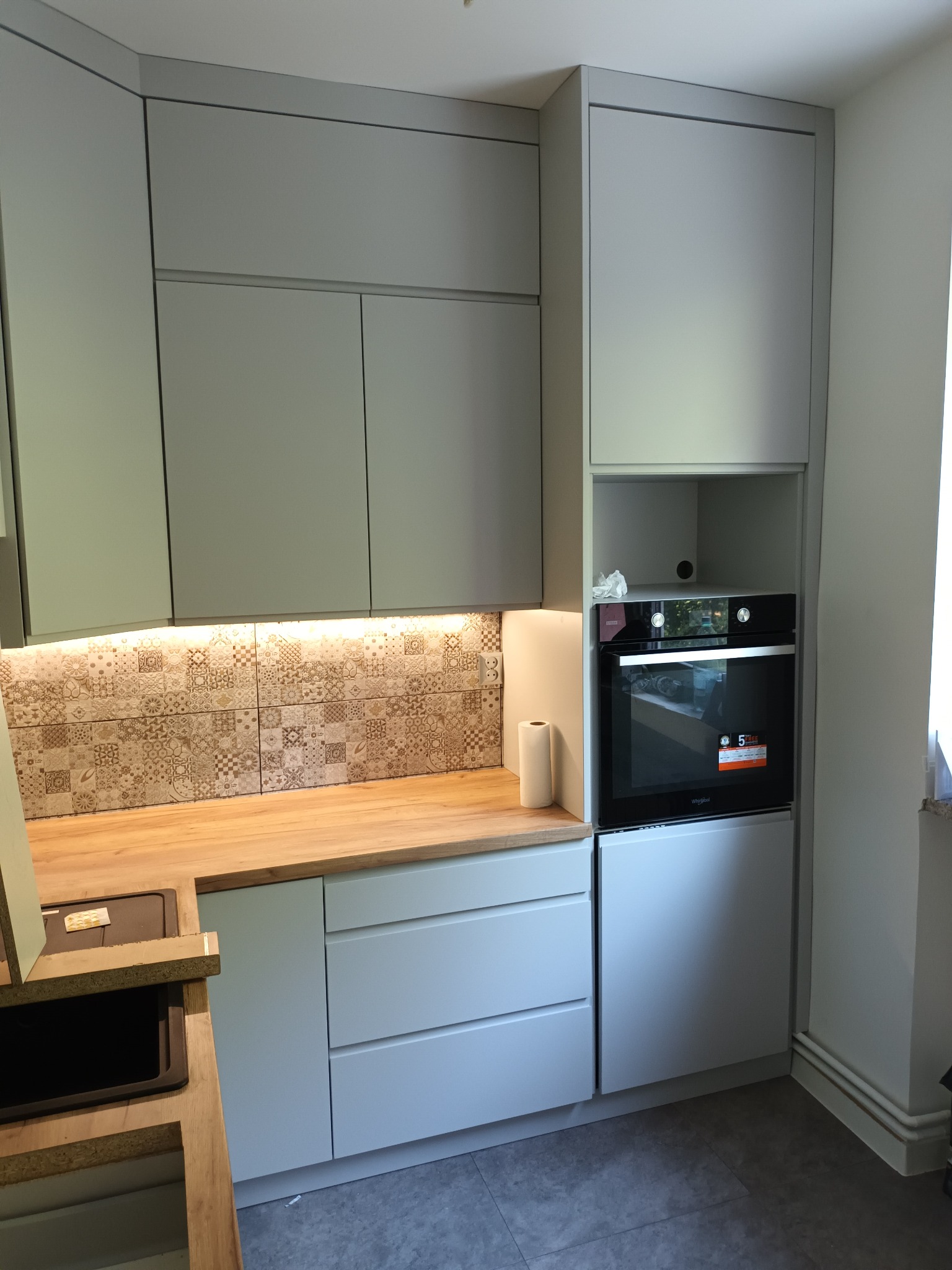 Nowoczesna kuchnia w odcieniach szarości z drewnianym blatem, ozdobnymi płytkami nad blatem i wbudowanym piekarnikiem Whirlpool.