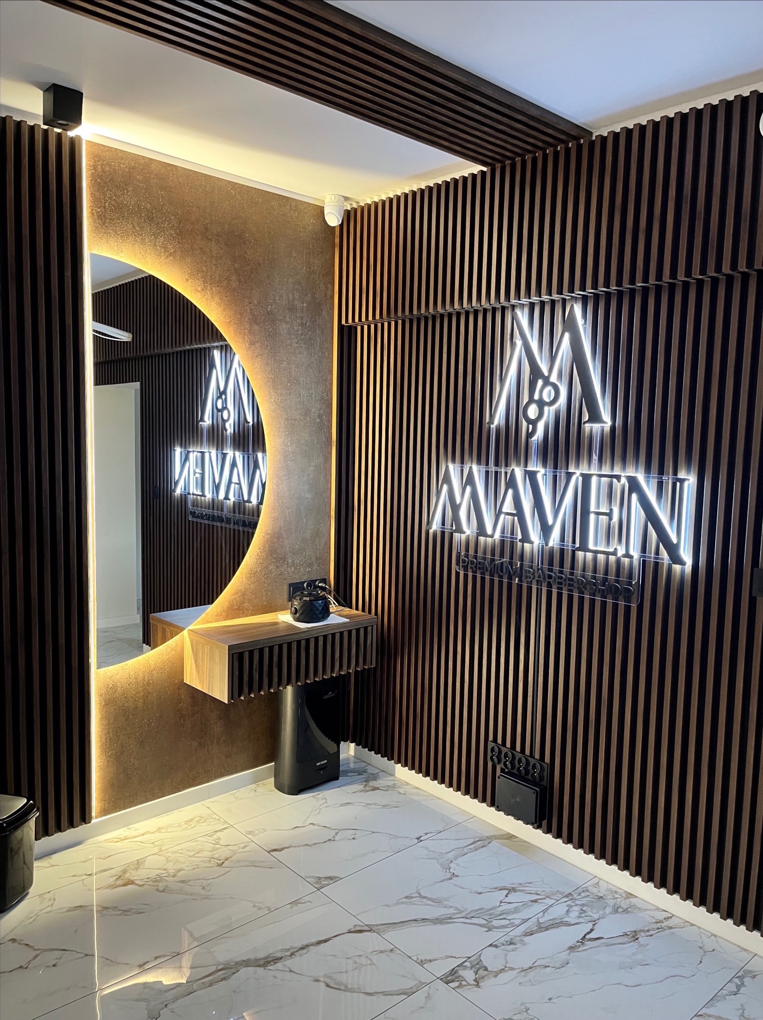Salon barberski MAVEN: oświetlenie LED w lamelach, brama ledowa, nagłośnienie sufitowe. Nowoczesny design z drewnianymi lamelami i marmurową podłogą.