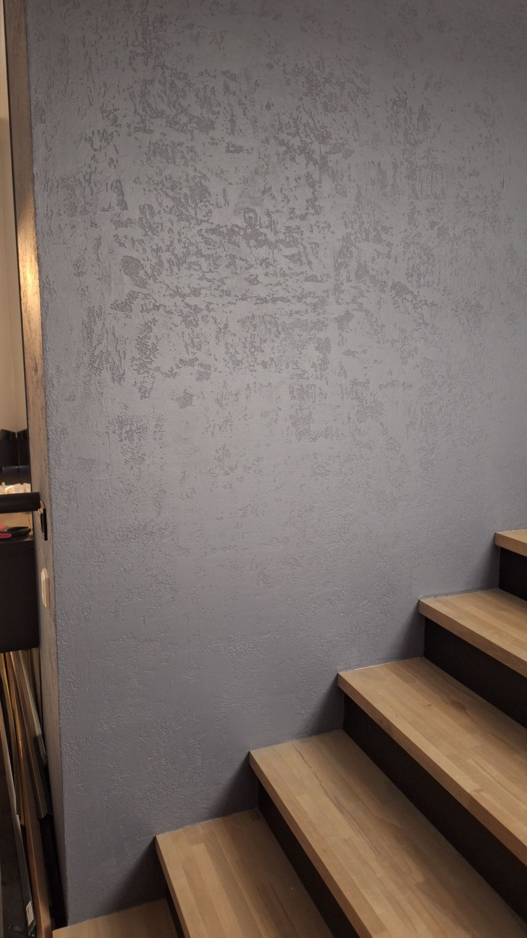 Dekoracyjna ściana ze strukturą w odcieniach szarości, widoczna obok drewnianych schodów we Włocławku. Efektowna aranżacja wnętrza.