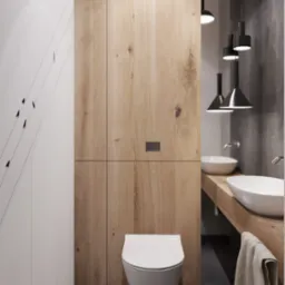 Nowoczesna łazienka z drewnianą zabudową, podwieszaną toaletą i umywalkami nablatowymi podświetlonymi przez designerskie lampy wiszące.