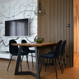 Jadalnia w Mogilanach z drewnianym stołem, czarnymi krzesłami i dekoracyjną ścianą z mapą miasta oraz panelami ściennymi.