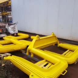 Elementy konstrukcyjne ze stali, świeżo pomalowane na żółto, leżące na ziemi przed białym budynkiem.