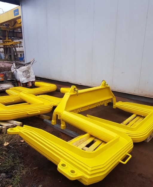 Elementy konstrukcyjne ze stali, świeżo pomalowane na żółto, leżące na ziemi przed białym budynkiem.