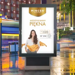 Miejski billboard z reklamą kosmetyków Mincer Pharma, prezentujący uśmiechniętą kobietę na tle białego tła z elementami złota, na mokrym chodniku z odbijającymi się światłami miasta.
