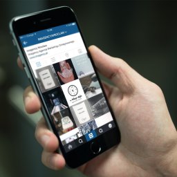 IMAGENCY Sp. z o.o. - Mężczyzna trzyma telefon wyświetlający profil agencji marketingowej na Instagramie, widoczny układ siatki z postami.