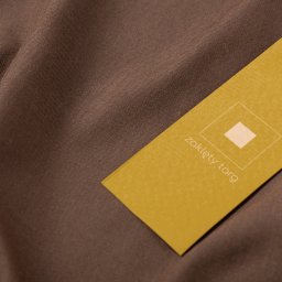 IMAGENCY Sp. z o.o. - Żółta etykieta z logo i tekstem 'zaklęty targ' zawieszona na brązowej tkaninie z widoczną fakturą.