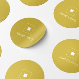 IMAGENCY Sp. z o.o. - Żółte, okrągłe naklejki z logo i nazwą 'zaklęty targ' ułożone na białym tle, jedna naklejka lekko odklejona.