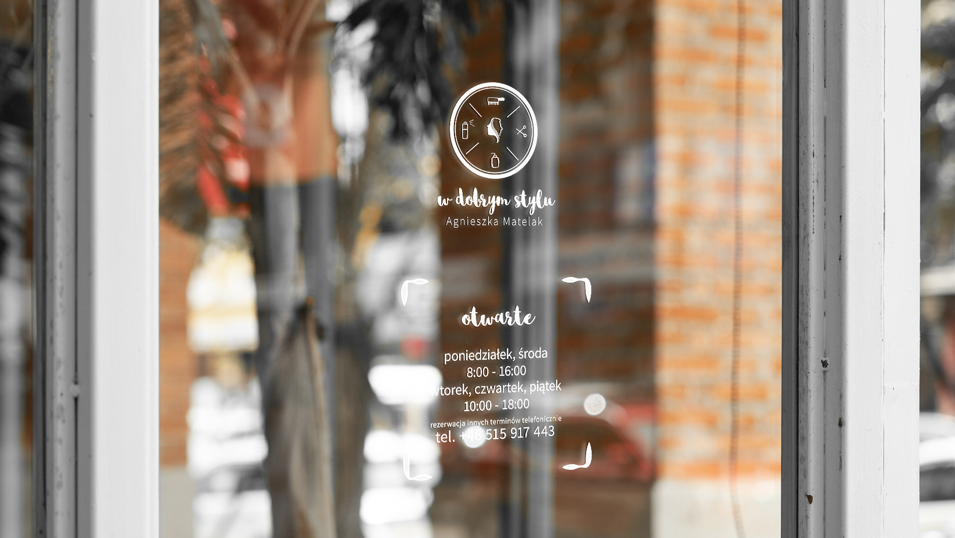 Wizytówka salonu fryzjerskiego z logo w okrągłej ramce, nazwa salonu 'W dobrym stylu Agnieszka Matelak' i godziny otwarcia naklejone na szklanych drzwiach wejściowych.