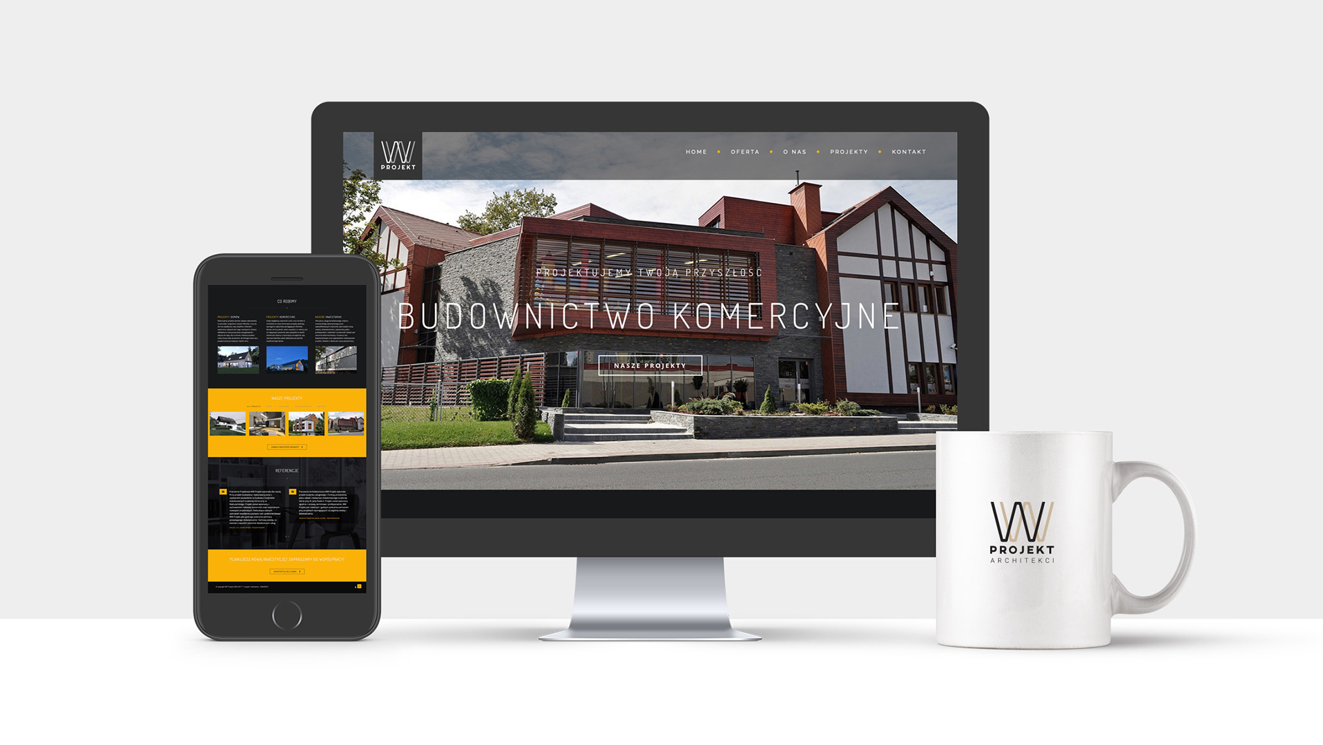 Prezentacja strony internetowej biura architektonicznego na monitorze i smartfonie, obok kubek z logo firmy.