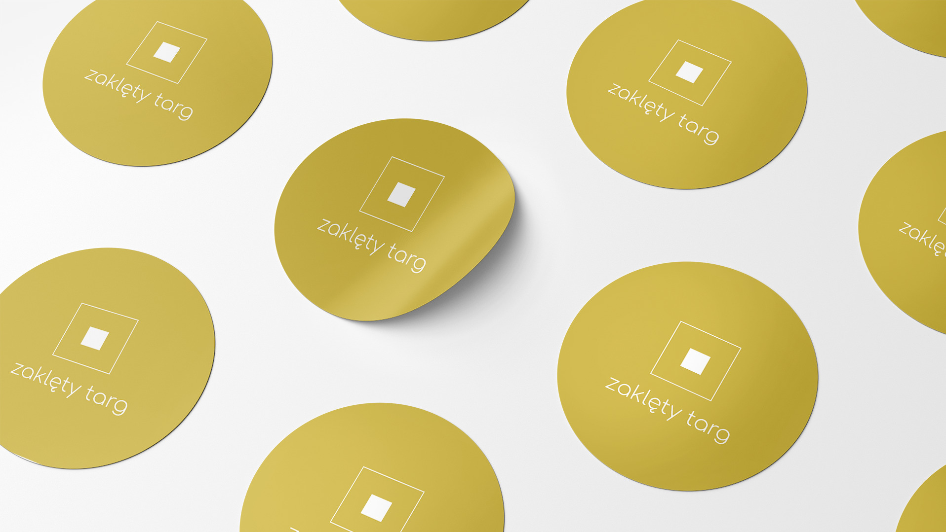 Żółte, okrągłe naklejki z logo i nazwą 'zaklęty targ' ułożone na białym tle, jedna naklejka lekko odklejona.