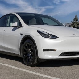 MIKAR MIKOŁAJ KARPIŃSKI - Biały samochód elektryczny Tesla Model Y z czarnymi felgami, zaparkowany na parkingu w słoneczny dzień, widoczny drugi samochód Tesla w tle.