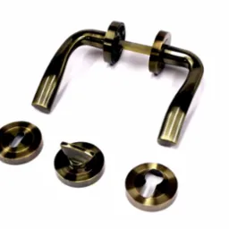 Zestaw klamki i szyldów w kolorze starego złota, widoczne elementy montażowe na białym tle.