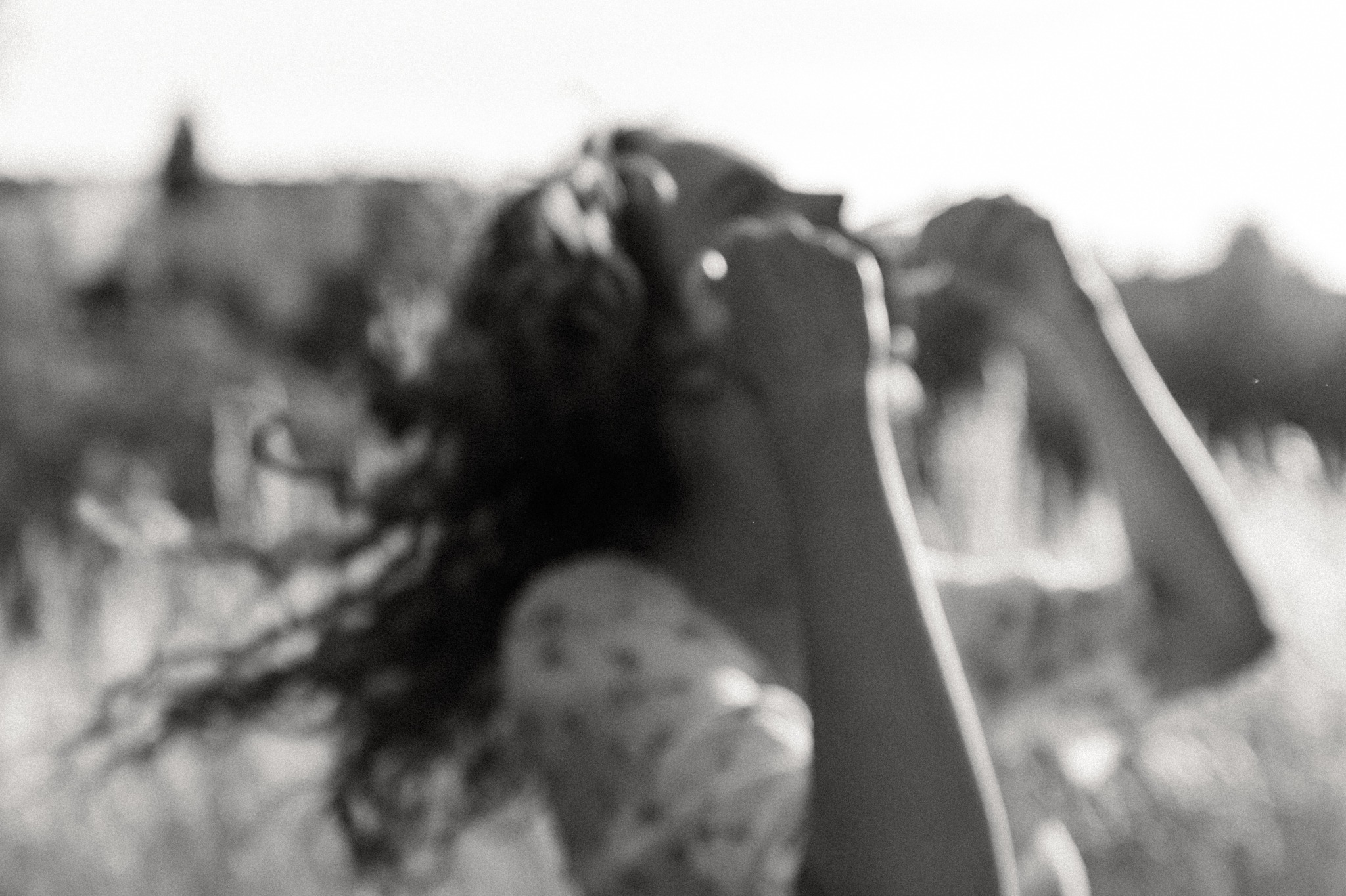 Rozmyte, czarno-białe ujęcie kobiety z rozwianymi włosami, ręce uniesione w górę, zarys krajobrazu w tle.