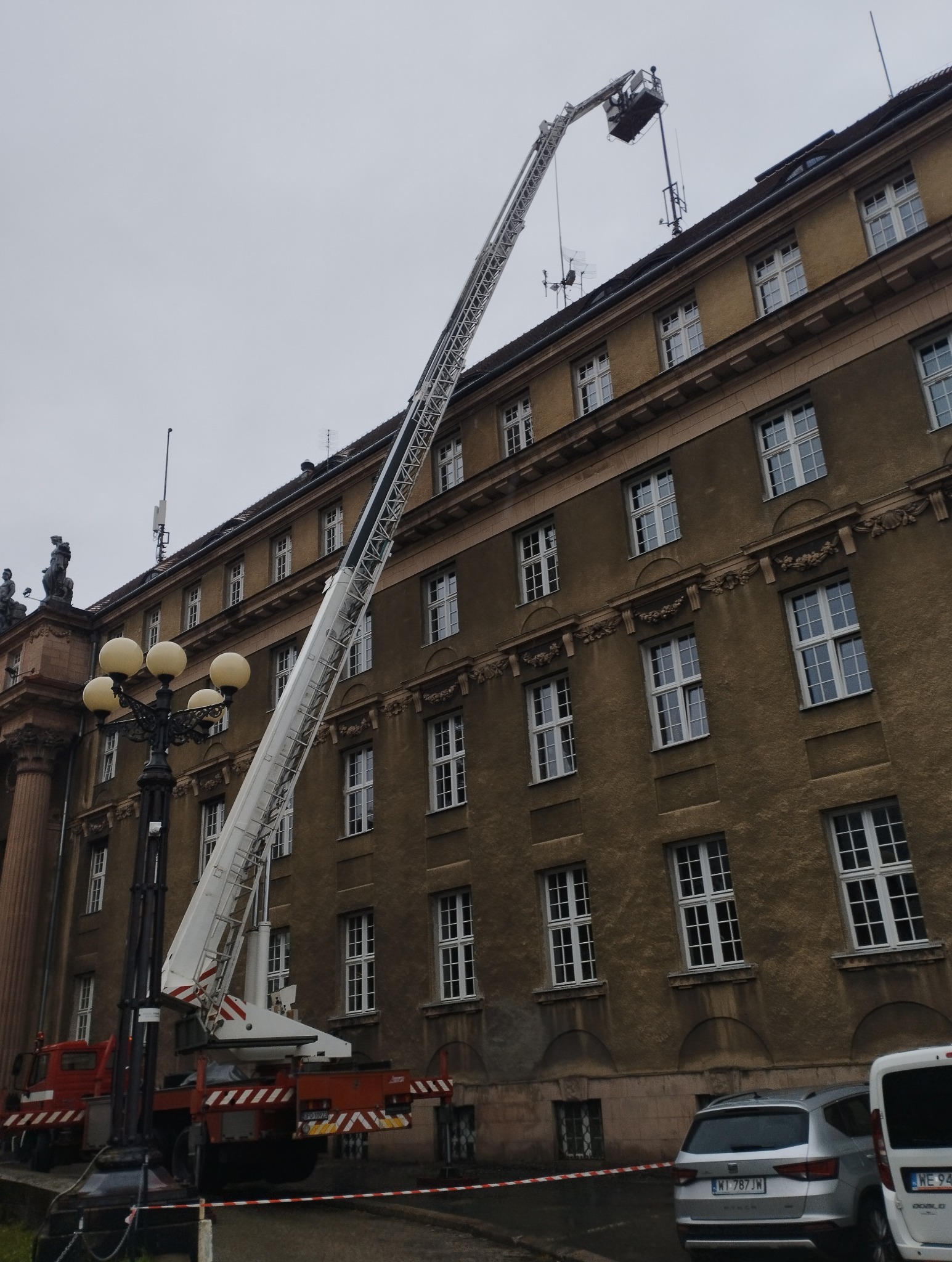 Kosz podnośnika ustawiony przy zabytkowej elewacji budynku, prawdopodobnie w trakcie prac konserwatorskich przy dachu.