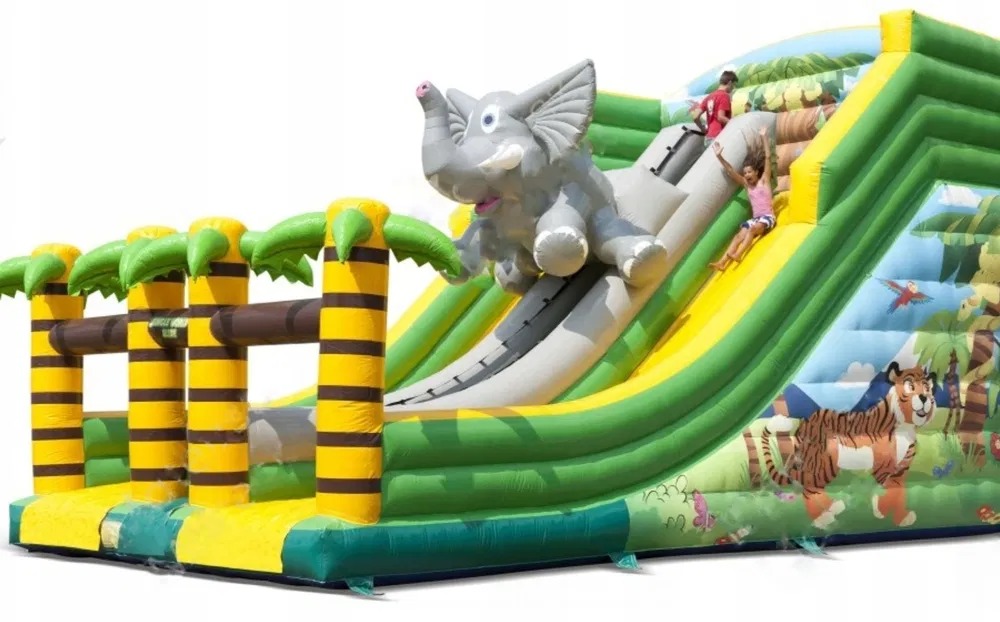Dmuchana zjeżdżalnia w stylu safari z motywem słonia, palm i tygrysa, dzieci zjeżdżające w dół.