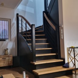 Holzmet s.c. S.Maślany, M. Maślany - Nowoczesne schody z czarnymi bokami i drewnianymi stopniami oraz metalową balustradą w jasnym wnętrzu. Widoczny fragment podłogi z desek i puszka farby w sprayu.