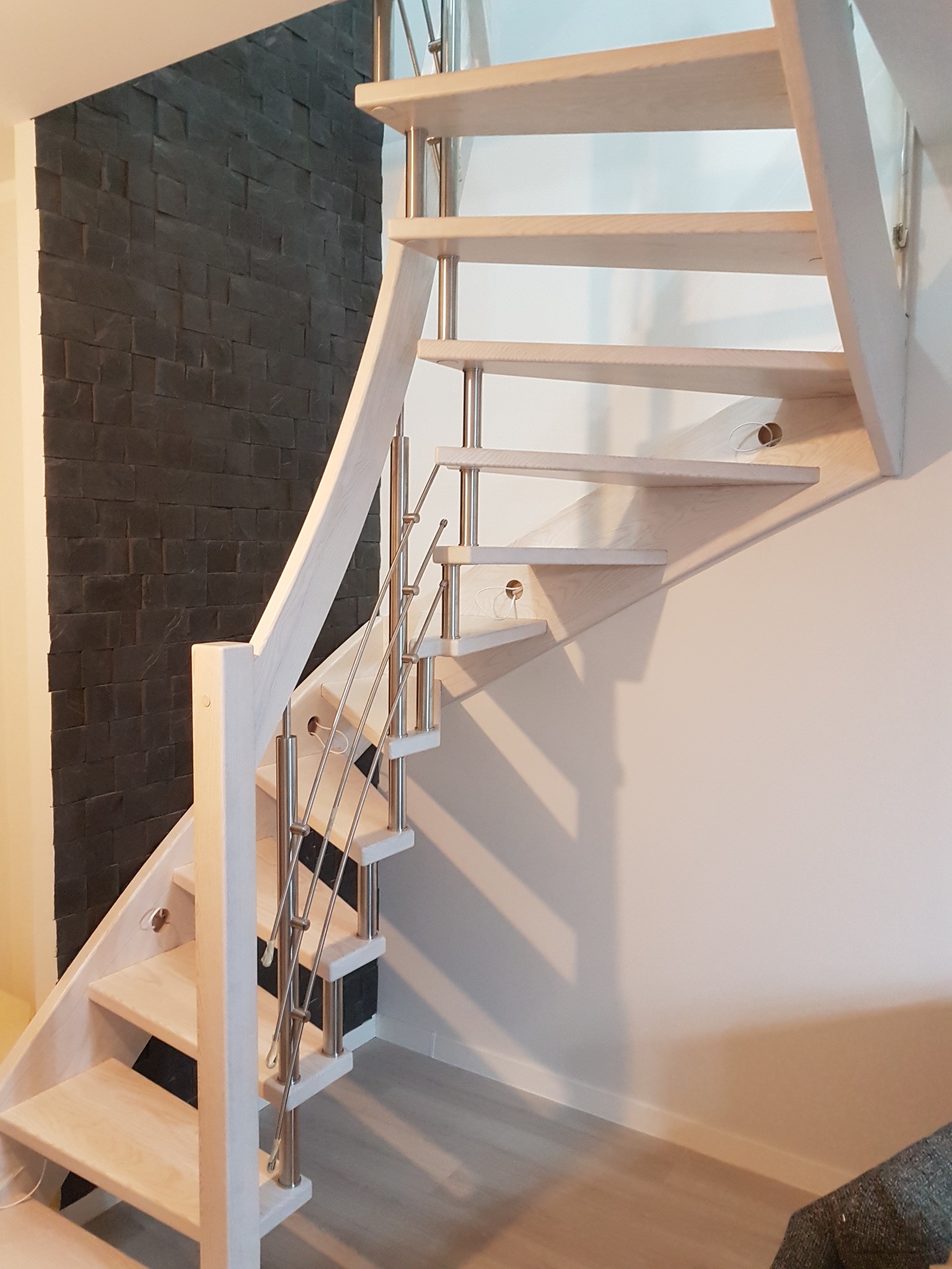 Jasne, drewniane schody z metalowymi barierkami, zamontowane przy ścianie z dekoracyjną, ciemną okładziną, widok z dołu.