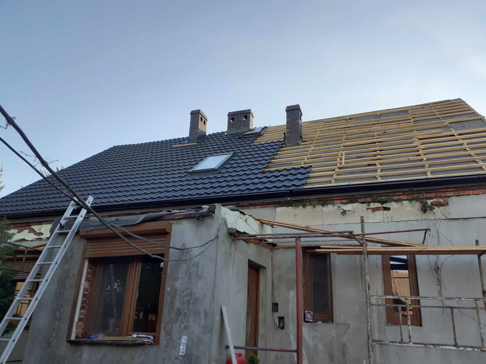 Częściowo ukończona konstrukcja dachu z nową blachodachówką i oknem dachowym, widoczne łaty pod kolejną część poszycia, trzy kominy, drabina oparta o budynek.