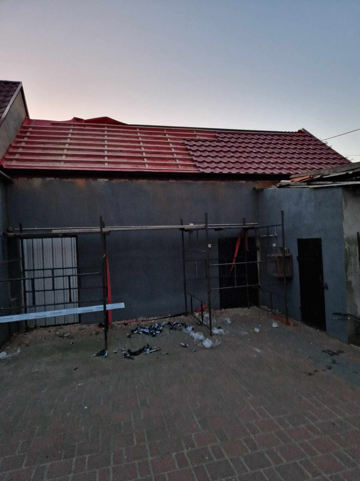 Częściowo pokryty dach z czerwonej blachodachówki, widoczne rusztowania i śmieci na podwórku, budynek w trakcie prac remontowych.