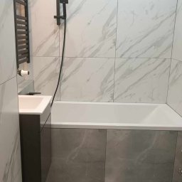 Mać Iek - Nowoczesna łazienka z wanną obudowaną szarymi płytkami, kabiną prysznicową w kolorze czarnym, umywalką z szarą szafką i grzejnikiem drabinkowym.