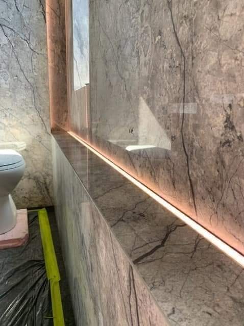 Półka z marmuru z podświetleniem LED w łazience w trakcie remontu, widoczna toaleta i folia ochronna na podłodze.