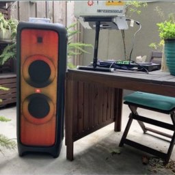 Daria Pisklova - Głośnik JBL Partybox obok stołu DJ-skiego z laptopem i gramofonami na zewnątrz, otoczenie rośliny doniczkowe i drewniane ogrodzenie.