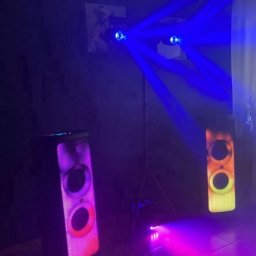 Daria Pisklova - Dwa głośniki JBL PartyBox z podświetleniem LED, oświetlenie sceniczne z niebieskimi promieniami, ciemne tło, płytki podłogowe.