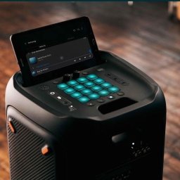 Daria Pisklova - Czarny głośnik imprezowy z podświetlanymi na niebiesko przyciskami i tabletem Samsung wyświetlającym listę utworów, ustawiony na drewnianej podłodze.