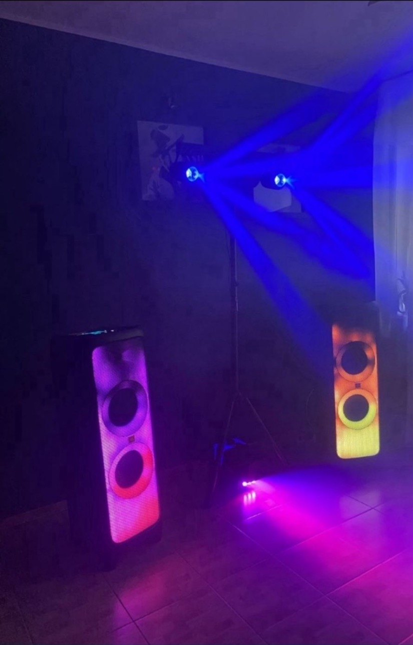 Dwa głośniki JBL PartyBox z podświetleniem LED, oświetlenie sceniczne z niebieskimi promieniami, ciemne tło, płytki podłogowe.