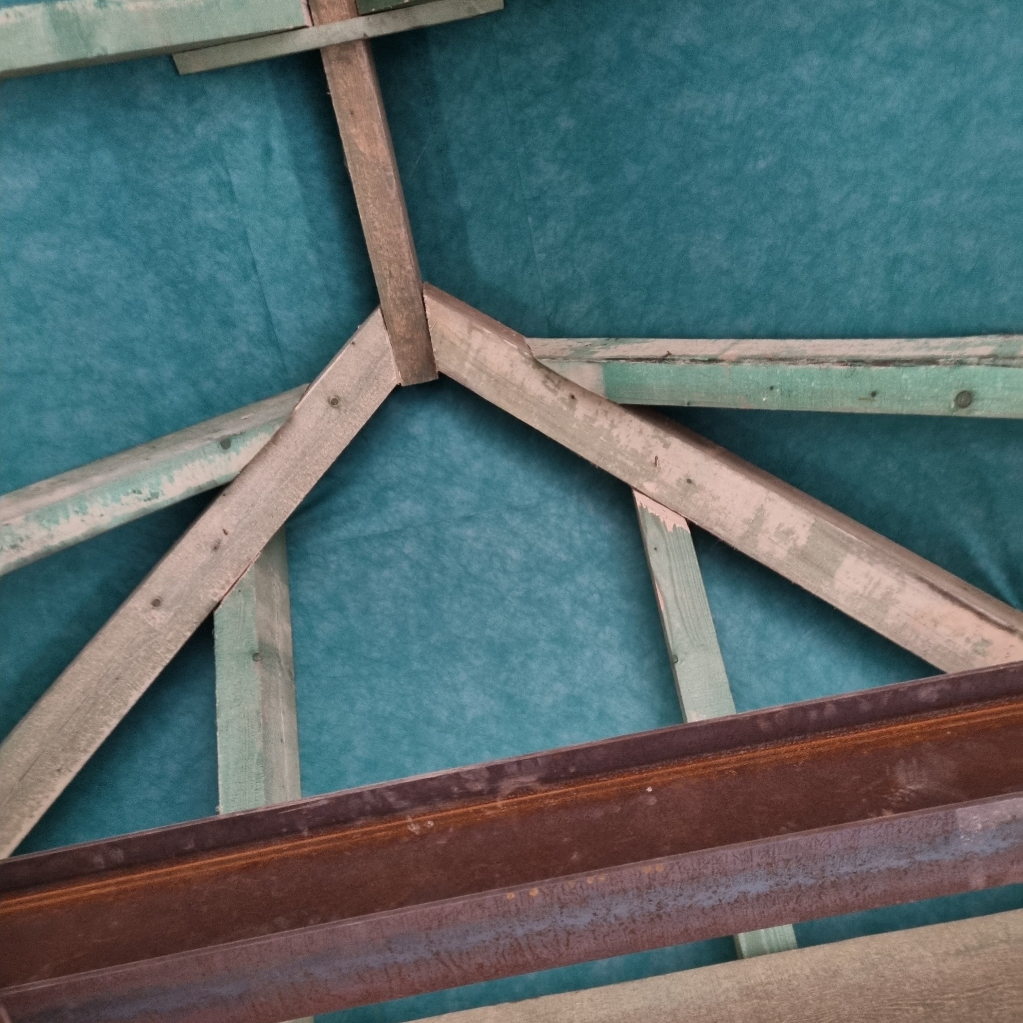 Drewniana więźba dachowa z elementami stalowymi na tle zielonej membrany dachowej, widok od wewnątrz.