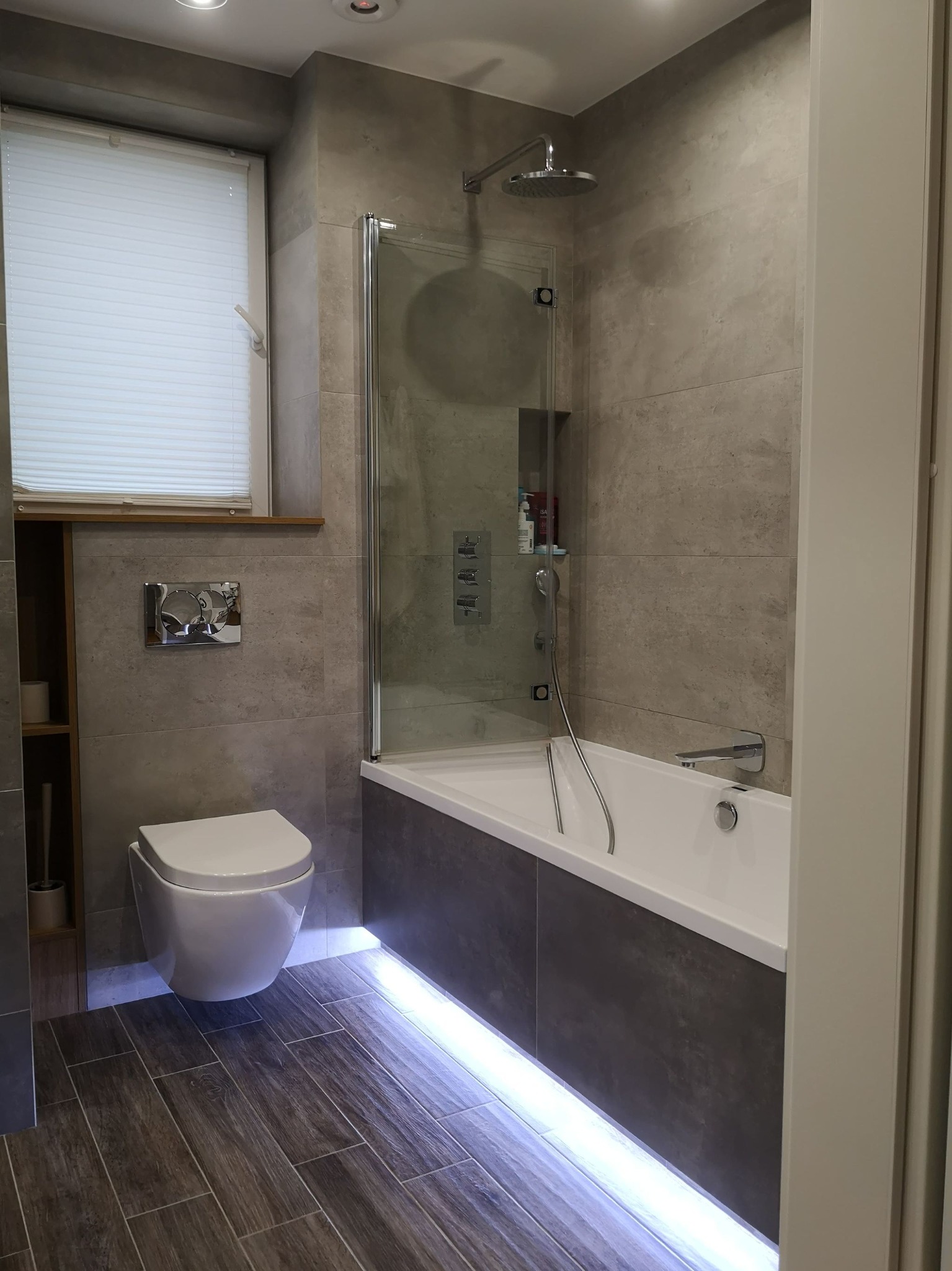 Nowoczesna łazienka w odcieniach szarości z podświetlaną wanną, wiszącą toaletą i deszczownicą