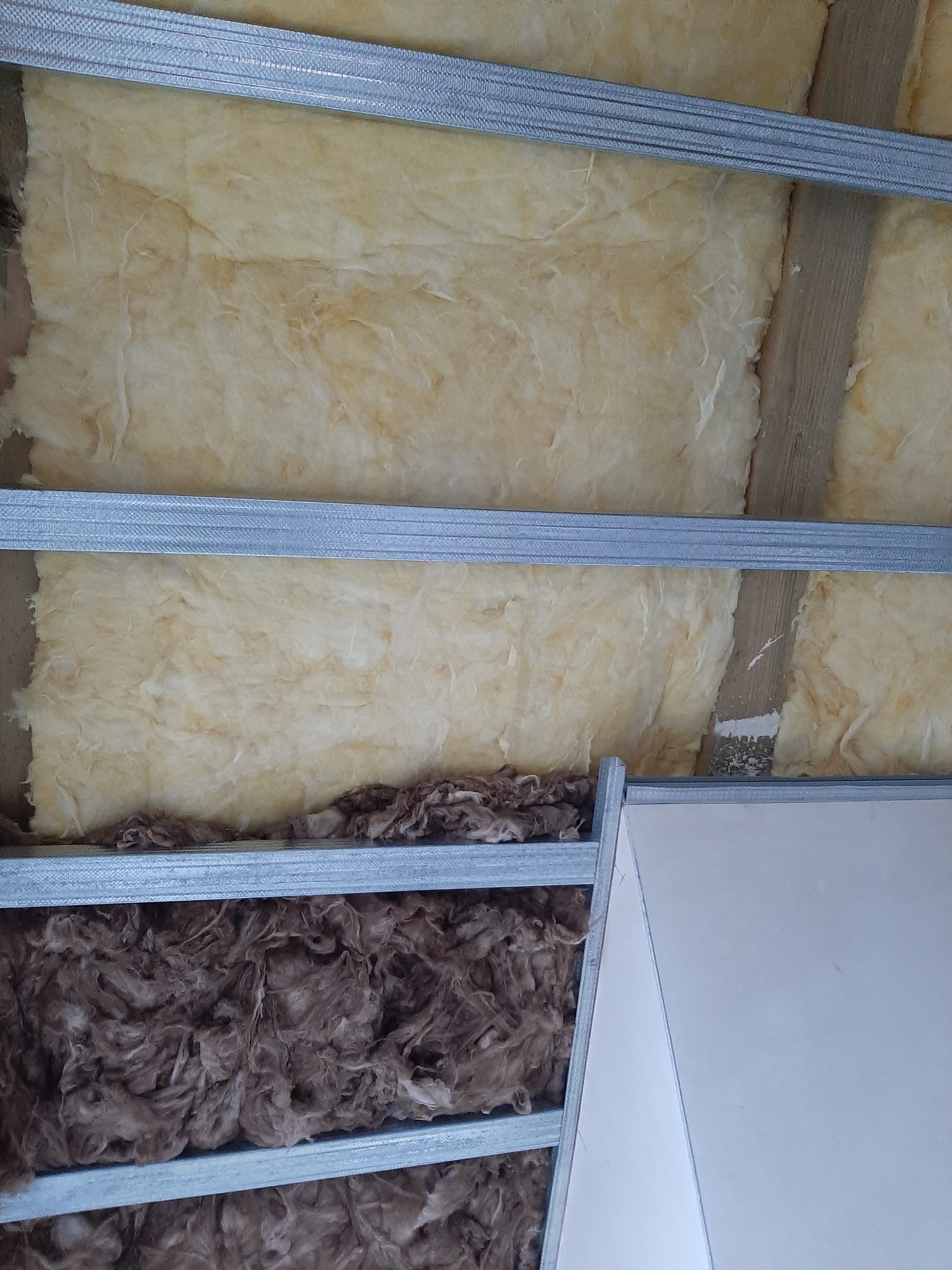 Ocieplenie poddasza wełną mineralną w metalowym stelażu, widoczna również płyta gipsowo-kartonowa.