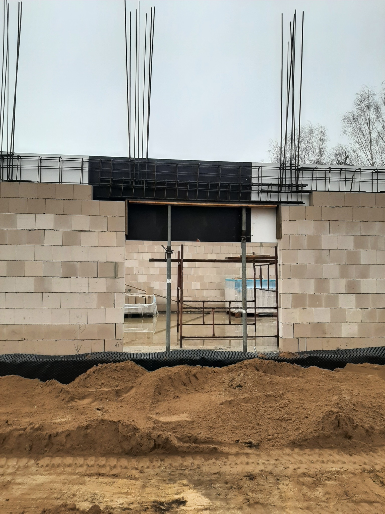 Wznoszenie ściany z bloczków betonowych na fundamencie z widocznym zbrojeniem pionowym i poziomym, z zabezpieczeniem hydroizolacyjnym przy gruncie.