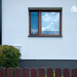 Damian Wesołowski - Fragment ocieplonej elewacji domu z brązowym oknem i widocznym logo firmy Wojtmar Dajemy Energię! w prawym górnym rogu.