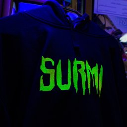 MTDesign Michał Tarnaski - Czarna bluza z kapturem z jaskrawozielonym napisem 'SURMI' w stylu gotyckim, oświetlona niebieskim światłem.