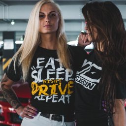 MTDesign Michał Tarnaski - Dwie kobiety pozują w czarnych koszulkach z nadrukami na tle parkingu podziemnego i czerwonego samochodu. Kobieta z blond włosami ma tatuaż na ramieniu i koszulkę z napisem 'EAT SLEEP NIGHT DRIVE...