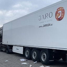 MTDesign Michał Tarnaski - Biała naczepa ciężarówki z dużym logo firmy transportowej JARO, widoczne koła i fragment kabiny, na ziemi leżą resztki folii po naklejeniu logo.