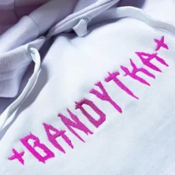 Biała bluza z kapturem, na której wykonano haft w kolorze fuksji z napisem 'BANDYTKA' pisanym charakterystyczną czcionką przypominającą zadrapania.
