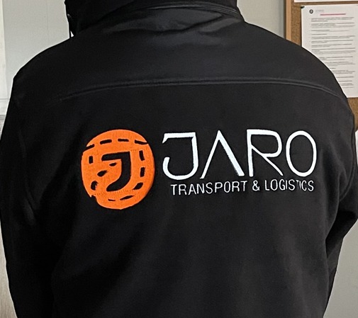 Czarna kurtka robocza z haftowanym logo firmy transportowej JARO na plecach, widok z tyłu.