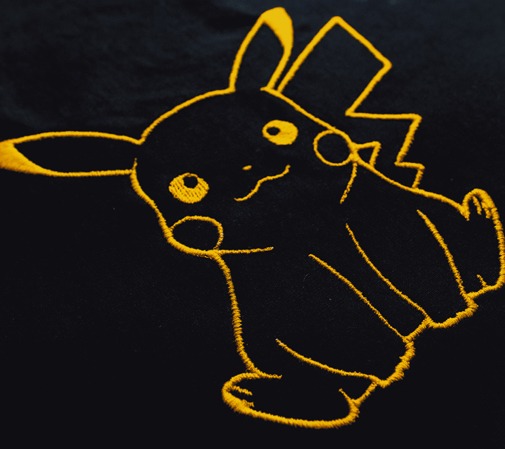 Ciemna tkanina z wyhaftowanym żółtą nicią wizerunkiem Pikachu.
