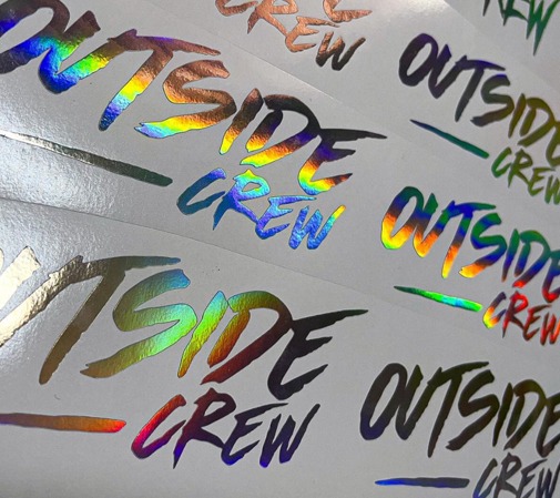 Arkusz z naklejkami 'Outside Crew' z efektem holograficznym w różnych kolorach, ułożone rzędami na białym tle.