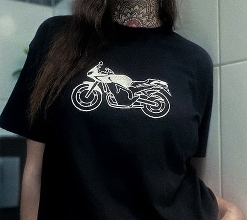 Czarna koszulka z białym, konturowym nadrukiem motocykla sportowego, widoczny tatuaż na szyi modelki z motywem mandali.