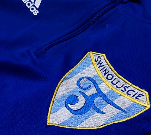 Niebieska bluza sportowa marki Adidas z haftowanym herbem Świnoujścia w lewym górnym rogu, widoczne logo producenta.