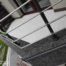 RAF-STONE Rafał Ćwierz - Barierka balkonowa ze stali nierdzewnej z czarnymi słupkami na balkonie wykończonym szarym kamieniem, widok z góry, drabina i plandeka w tle.