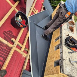 RAF-STONE Rafał Ćwierz - Prace dekarskie w toku: montaż blachy na dachu z widoczną konstrukcją drewnianą, narzędzia pracy i fragment sylwetki dekarza w odzieży roboczej.