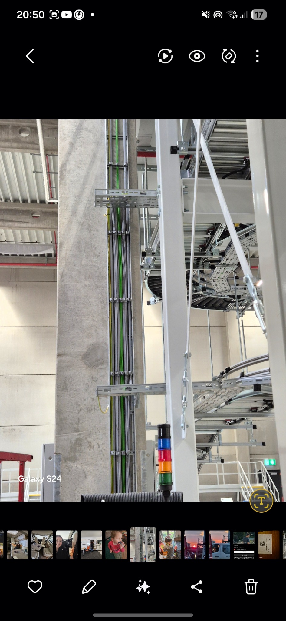 Wysoki słup z zamocowanymi kablami elektrycznymi w metalowych korytkach. Widoczne przewody w kolorach szarym, zielonym i żółtym. W tle konstrukcja z kablami.