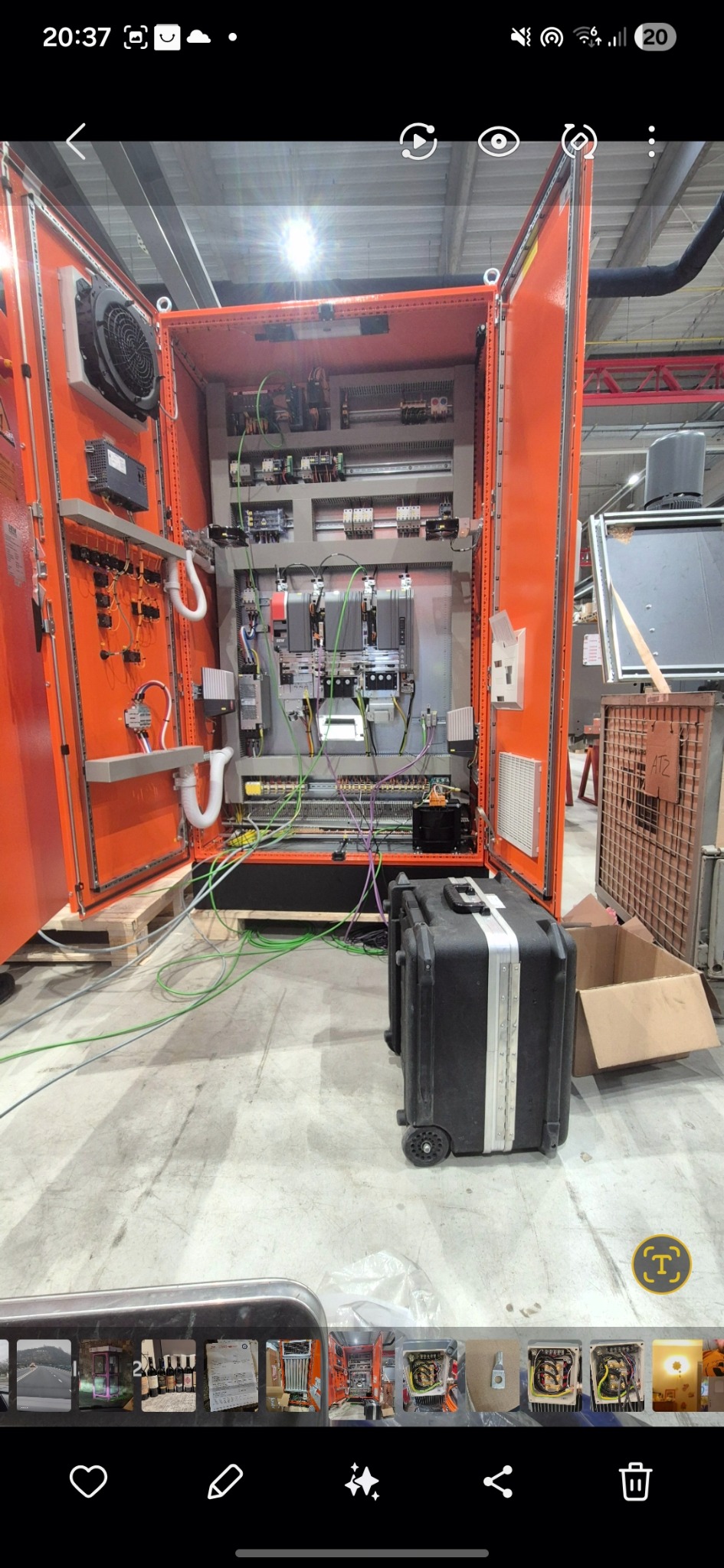 Otwarta, pomarańczowa szafa sterownicza z widocznymi elementami elektrycznymi i przewodami. Obok czarna skrzynia narzędziowa na kółkach. Widok z bliska na wnętrze szafy.