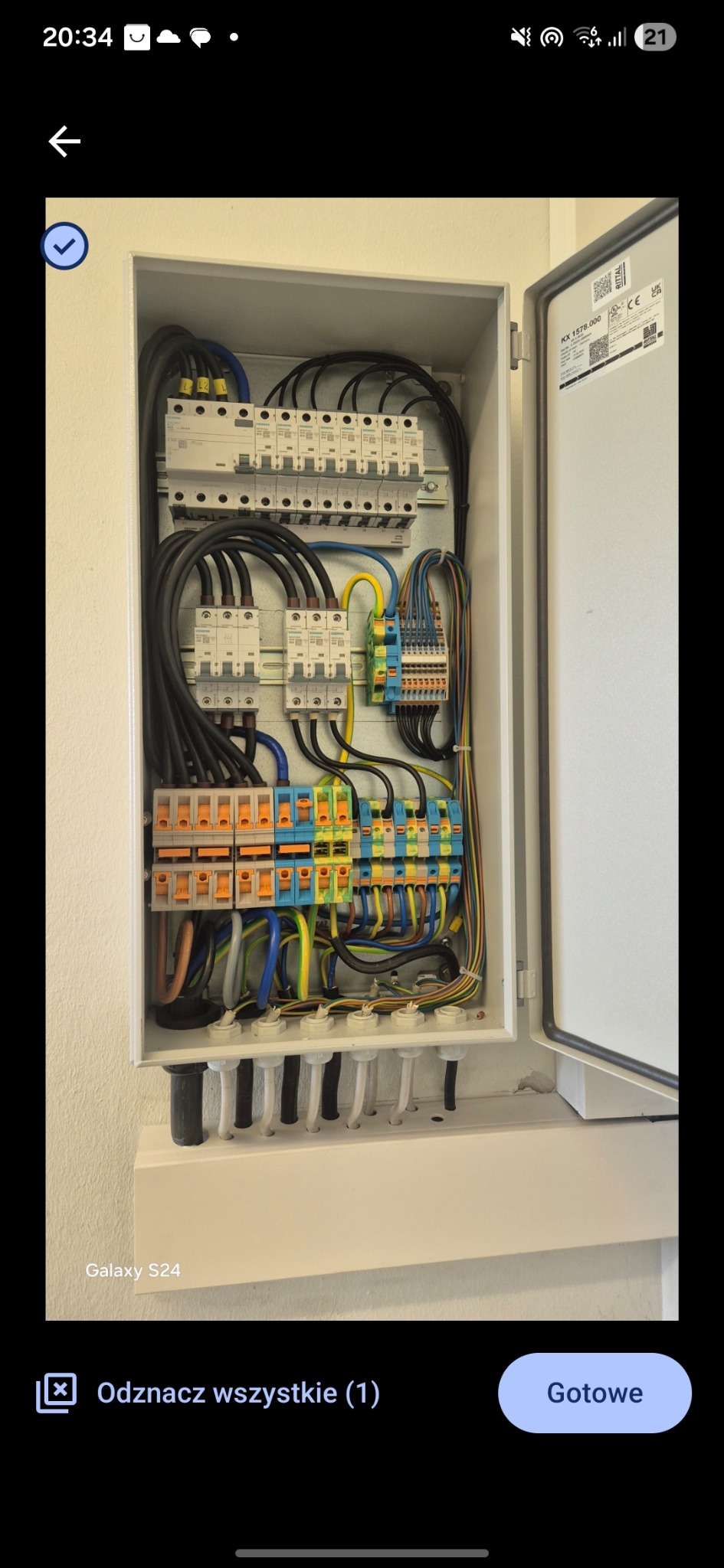 Otwarta skrzynka elektryczna z precyzyjnie ułożonymi przewodami, bezpiecznikami i złączkami. Widoczne czarne i kolorowe kable, listwy zaciskowe i elementy montażowe.