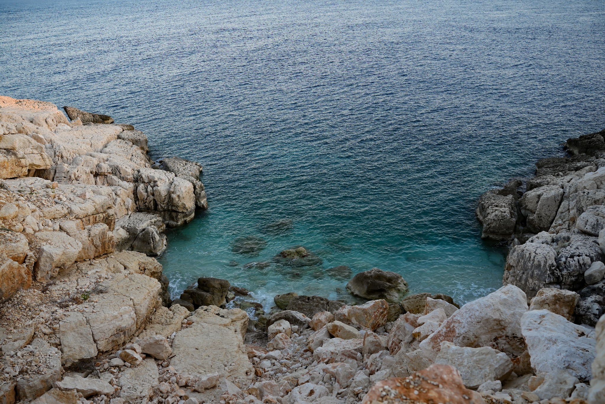 Turkusowa woda zatoki z białymi skałami i drobnymi falami morskimi.