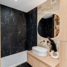ARCHITEKTURA WNĘTRZ Jakub Tarnowski - Nowoczesna łazienka z czarnymi płytkami imitującymi marmur, drewnianą szafką i owalnym lustrem z podświetleniem. Minimalistyczny design.